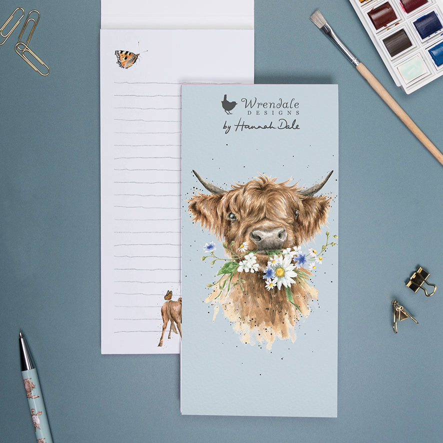 slim memo pad with picture of a highland cow on the front holding white daisies in his mouth.  The brand name wrendale designs by hannah dale is also on the fron tof the notepad.  The background behind the cow is pale blue in colour