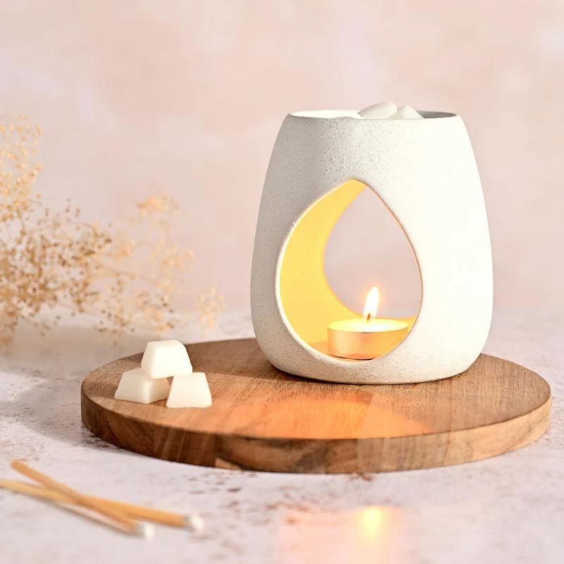 white stoneware wax melt burner displayed on a board with wax melts and a lit tealight candle