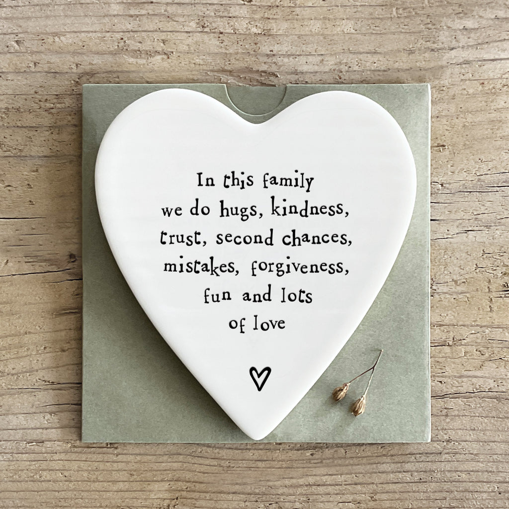 heart shape white porcelain drinks coaster featuring the words in the family we do hugs, kindness trust second chances mistakes forgiveness fun and lots of love in black text.  the coaster is displayed on a little paper sleeve