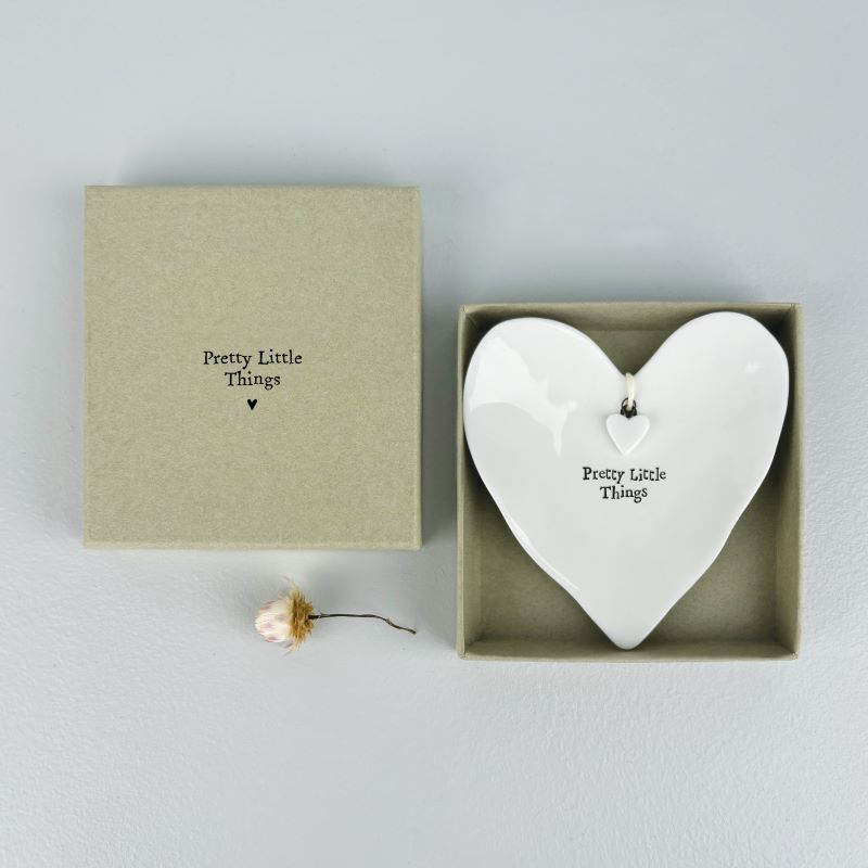 white porcelain heart shape ring dish with words pretty little things in black text on front.  There is a little hanging white porcelain heart in the centre of the dish.  The dish is in a sage green box with the words pretty little things on the outside