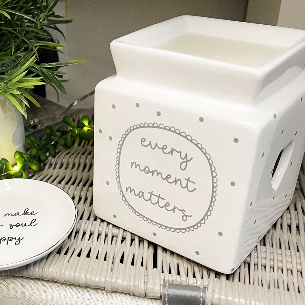 white ceramic wax melt oil burner with grey polka dot design and features the words every moment matters on the front.  There are heart cut outs on each side.  The wax melt burner is cube shaped with a square dish on top.