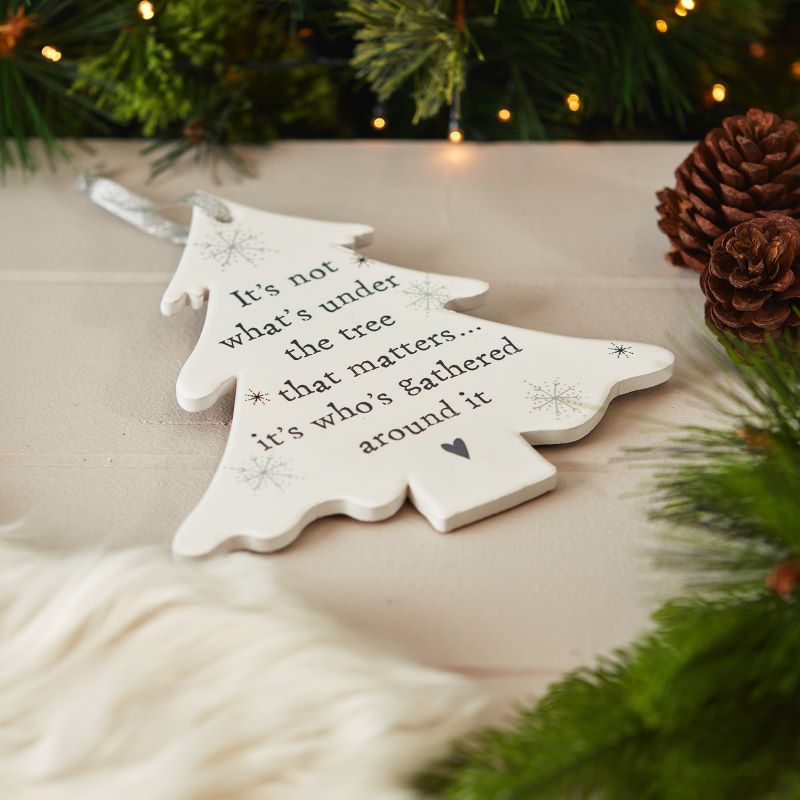 The white, ceramic Christmas tree hanging decoration features the words, 'It's not what's under the tree that matters... it's who's gathered around it.  The Christmas tree hanger is cork backed and is finished with a silver ribbon for hanging.